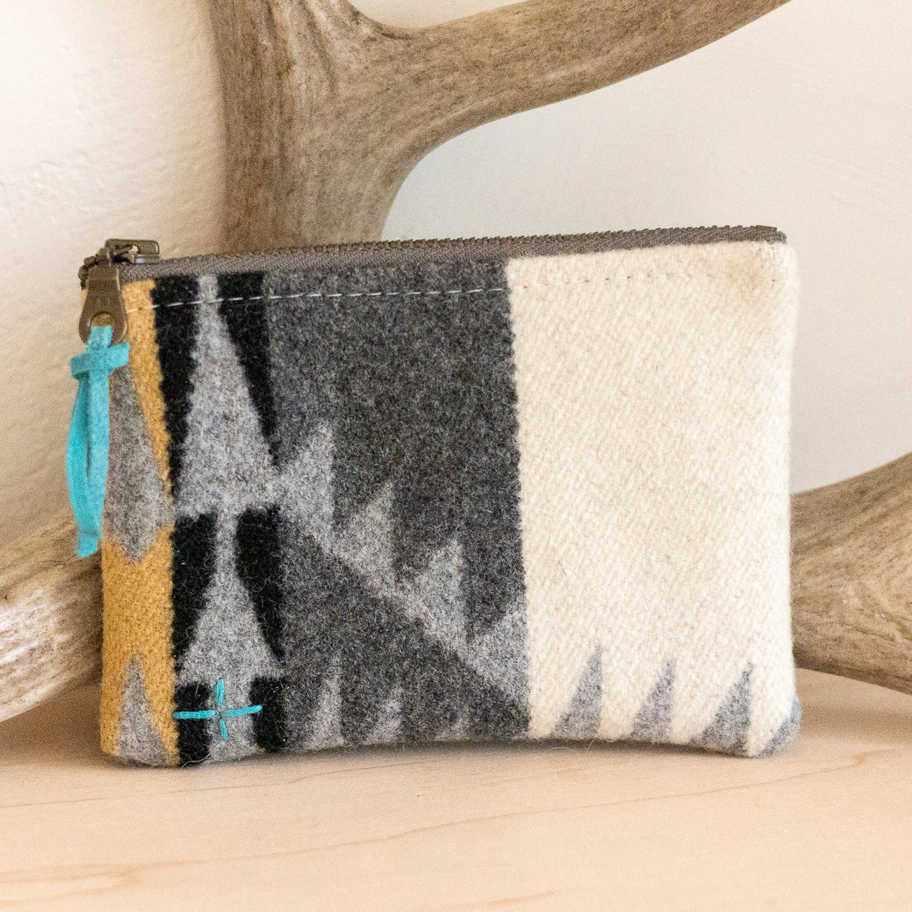 Woven pouch with geometric pattern on a wooden surface with antlers in the background