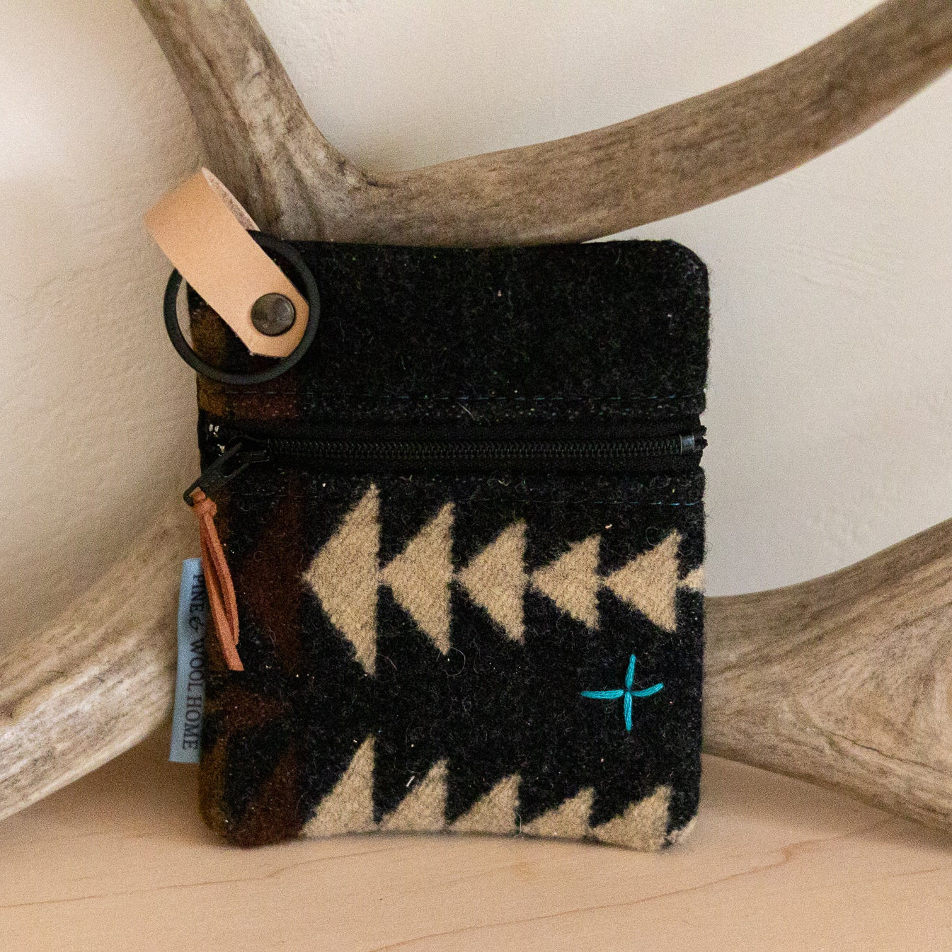 Black cardholder with beige pattern on a wooden surface with antlers