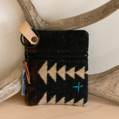 Black cardholder with beige pattern on a wooden surface with antlers