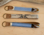 Three fabric keychains with leather ends on a wooden surface