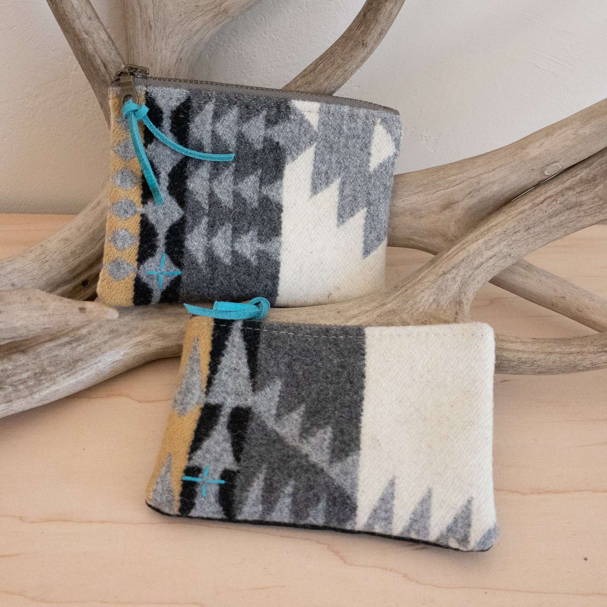 Two patterned pouches with blue accents on a wooden surface with antlers in the background
