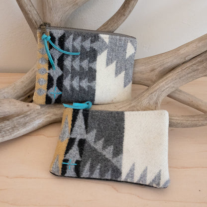 Two patterned pouches with blue accents on a wooden surface with antlers in the background