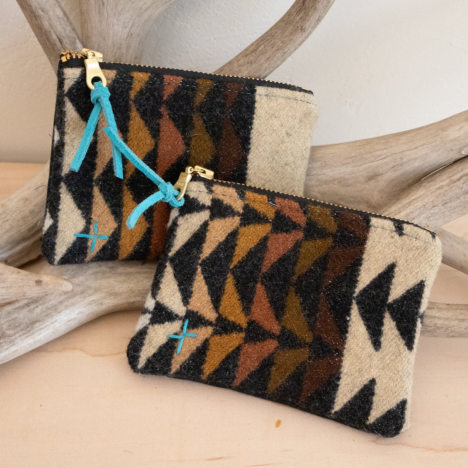 Two patterned pouches with a gold zipper on a wooden surface with antlers in the background.