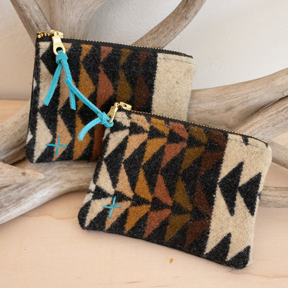 Two patterned pouches with a gold zipper on a wooden surface with antlers in the background.