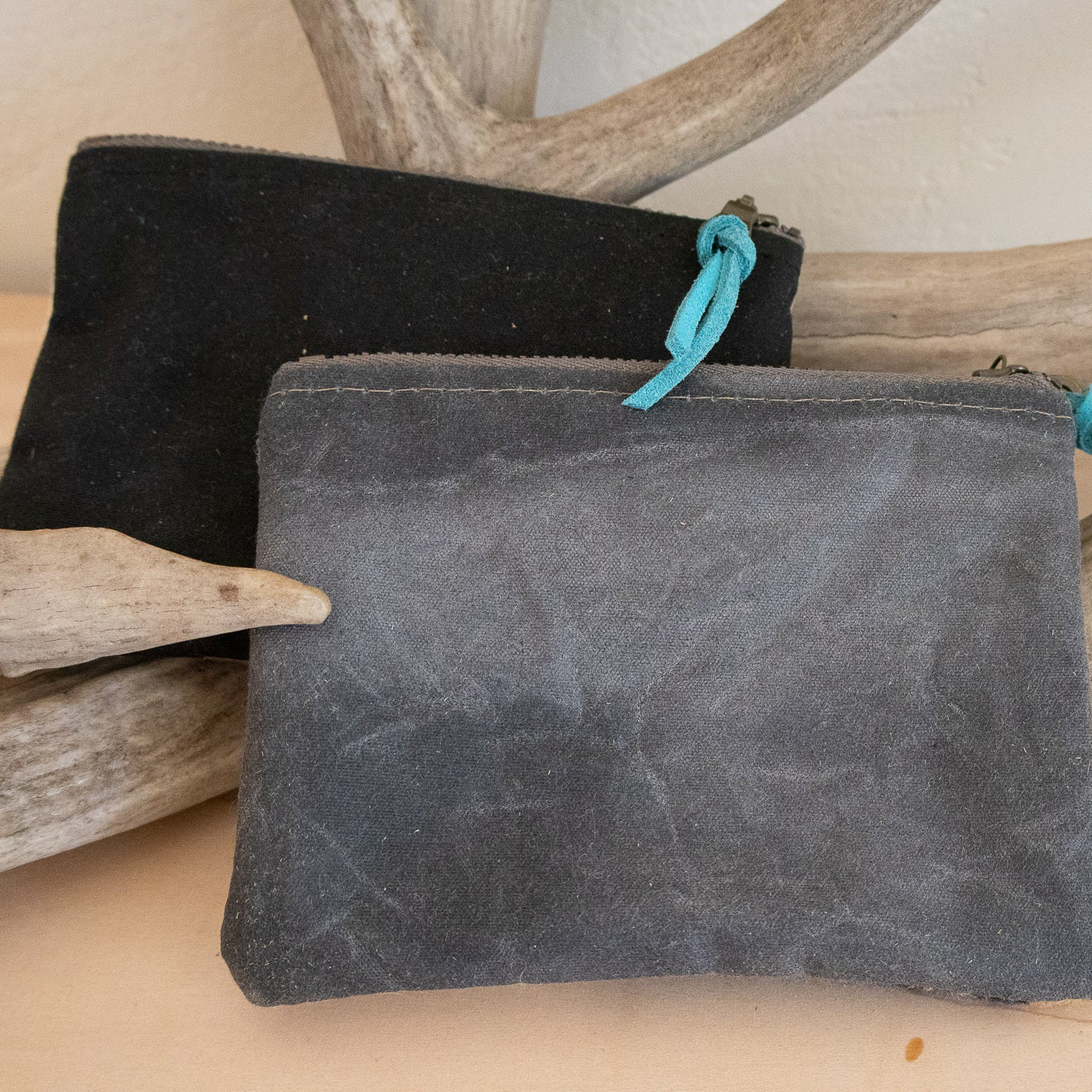Two suede pouches, one black and one gray, with turquoise drawstrings, on a wooden surface with driftwood.