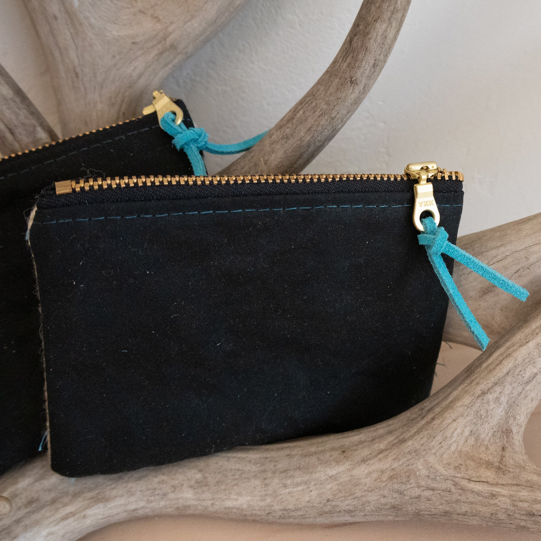 Black pouch with gold zipper and blue drawstrings on a wooden surface