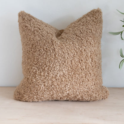 Textured beige pillow on a wooden surface with a light background
