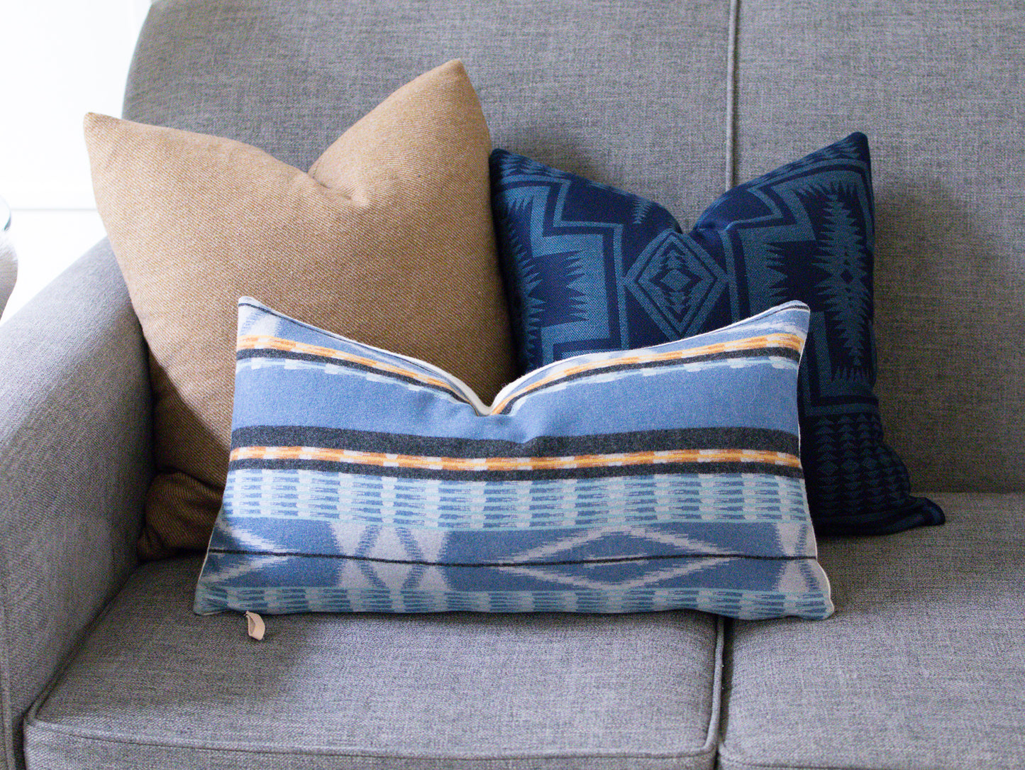 Three decorative pillows on a gray sofa, including a blue patterned pillow.