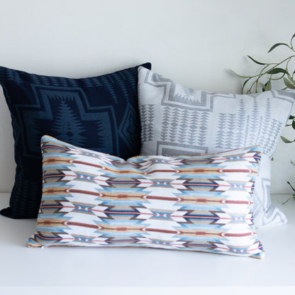 Three patterned pillows on a white surface with a plant in the background