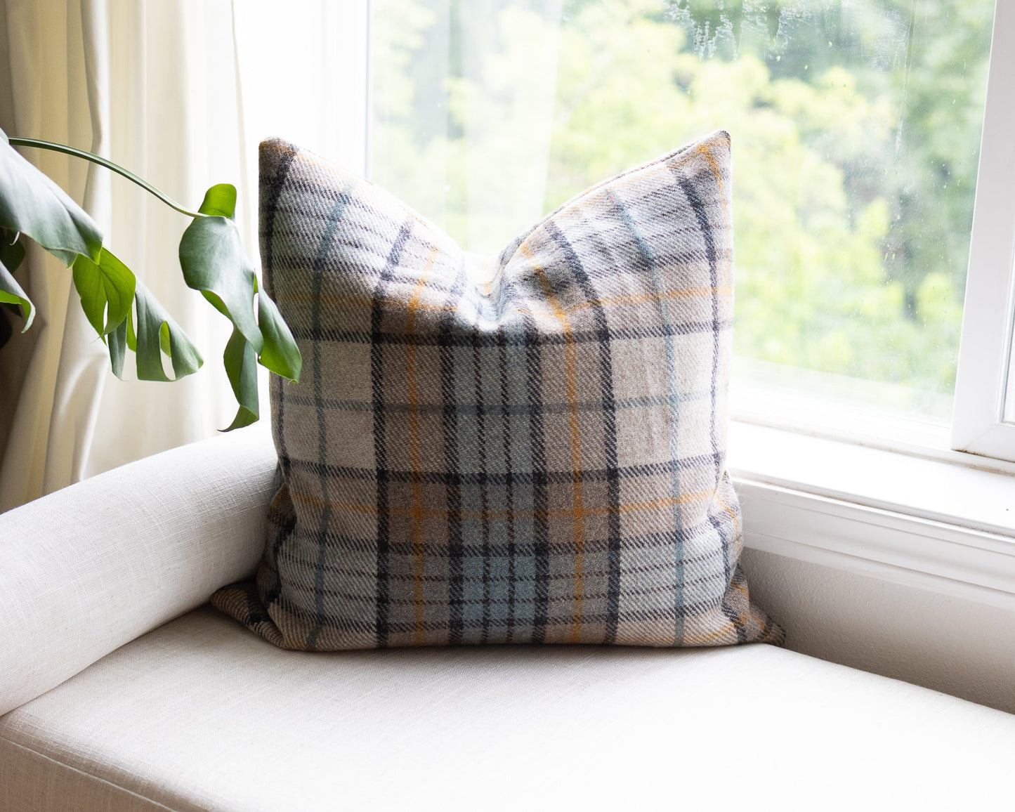 Plaid pillow on a white couch with a window and plant in the background