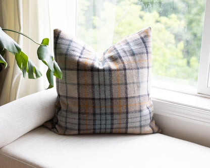 Plaid pillow on a white couch with a window and plant in the background