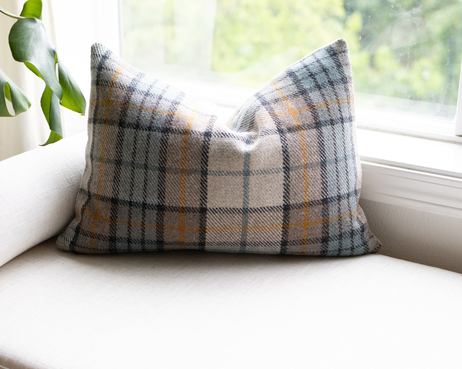 Plaid pillow on a white couch with a window and plant in the background