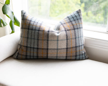 Plaid pillow on a white couch with a window and plant in the background