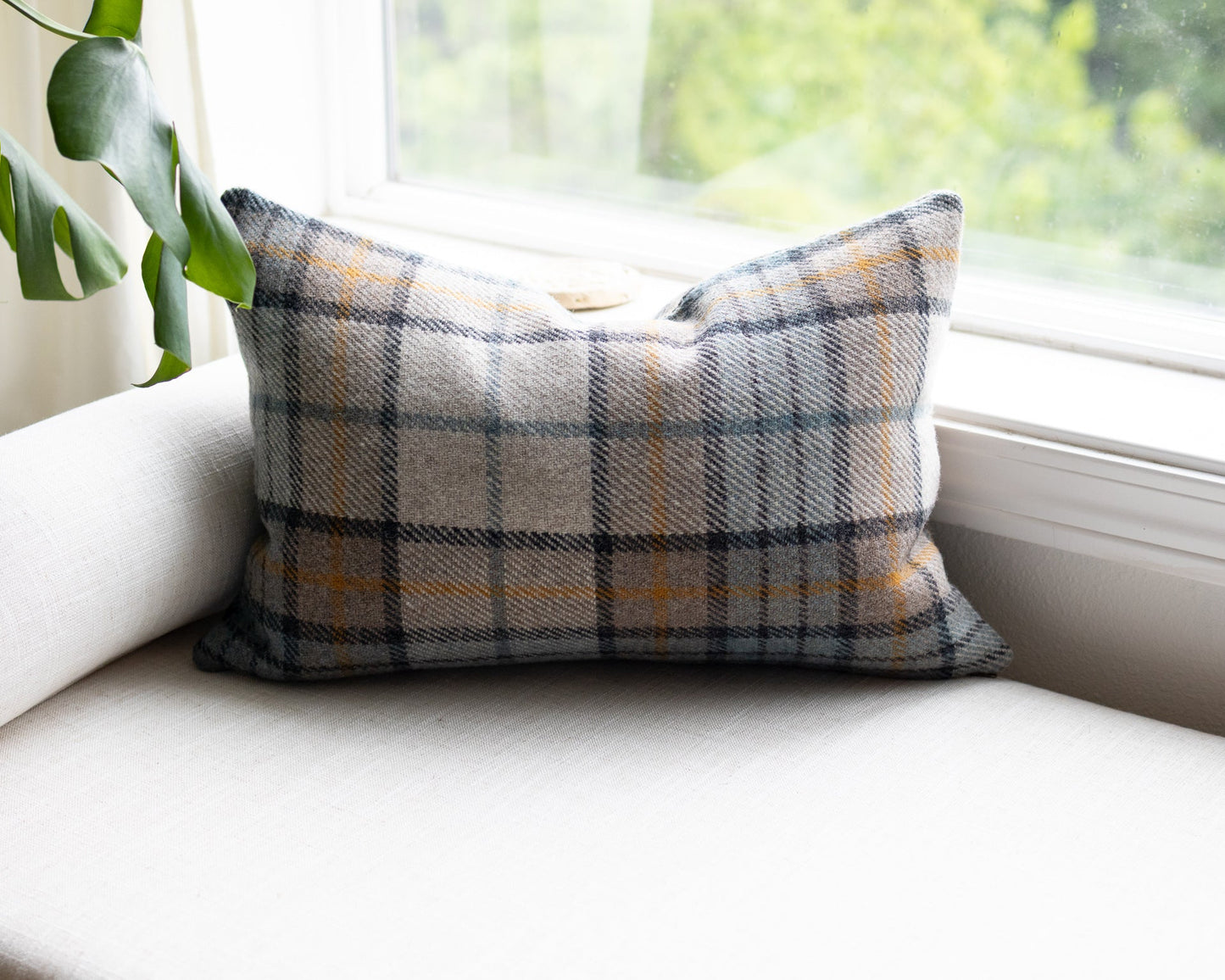 Plaid pillow on a white couch with a window and plant in the background
