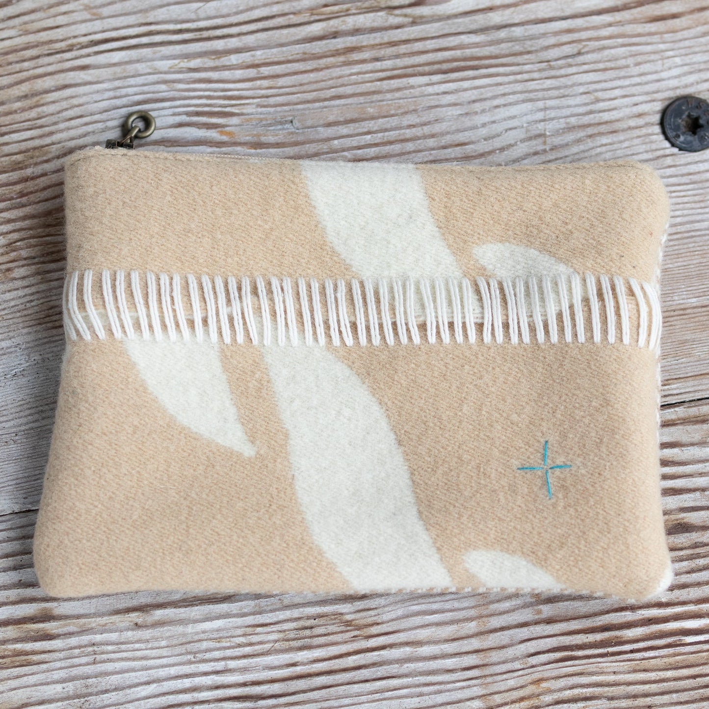 Beige pouch with white floral design and a comb on a wooden surface