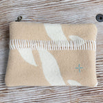 Beige pouch with white floral design and a comb on a wooden surface