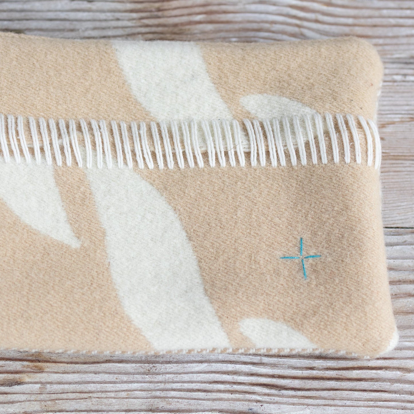 Beige and white blanket with fringe on a wooden surface