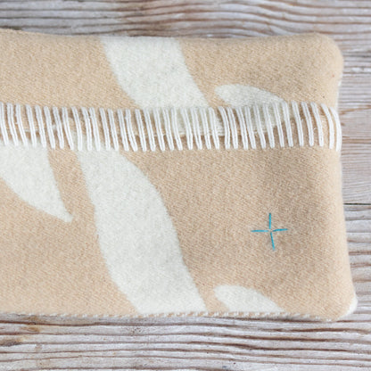 Beige and white blanket with fringe on a wooden surface