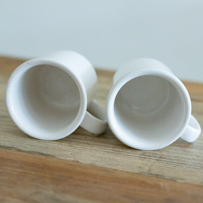 Two white ceramic mugs on a wooden surface with a light gray background