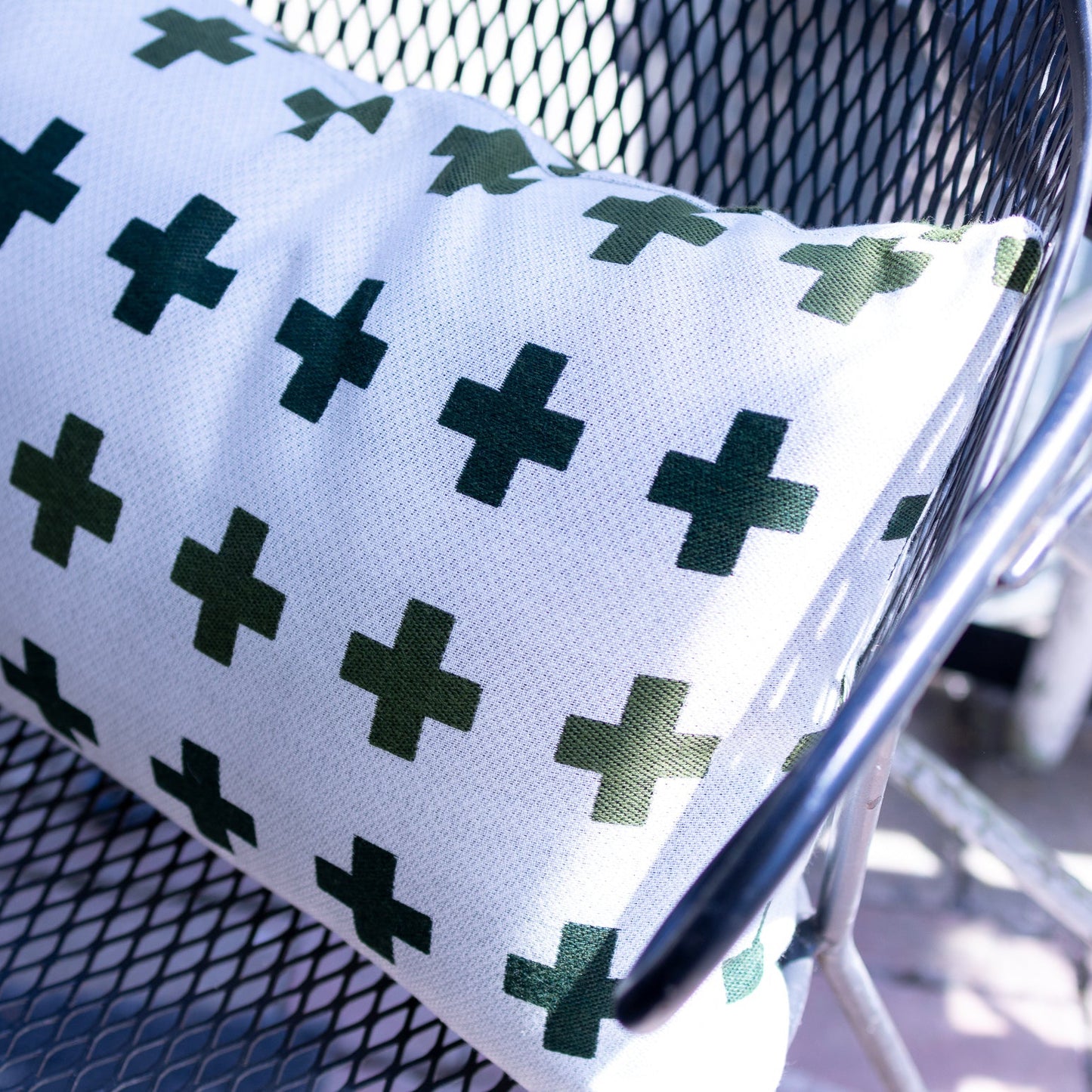 White pillow with green cross pattern on a chair