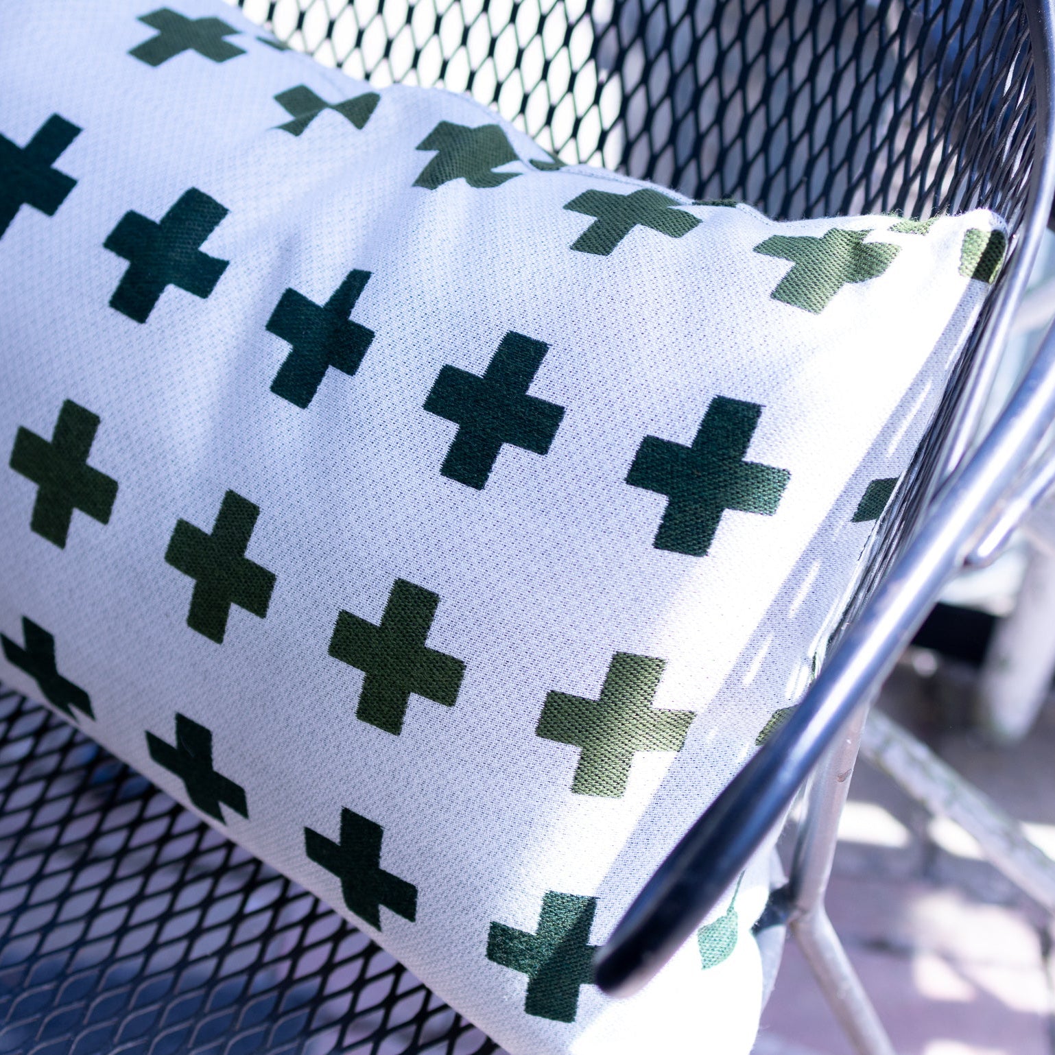 White pillow with green cross pattern on a chair