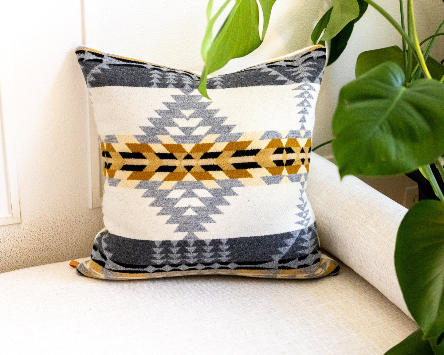 Decorative pillow with geometric pattern on a white couch with plants in the background