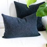 Two dark gray pillows on a white couch with green leaves in the foreground
