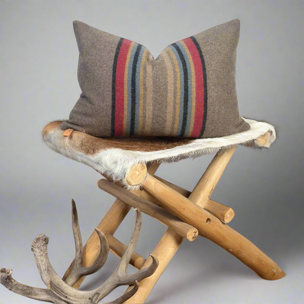 Decorative pillow with striped pattern on a wooden stool against a plain background