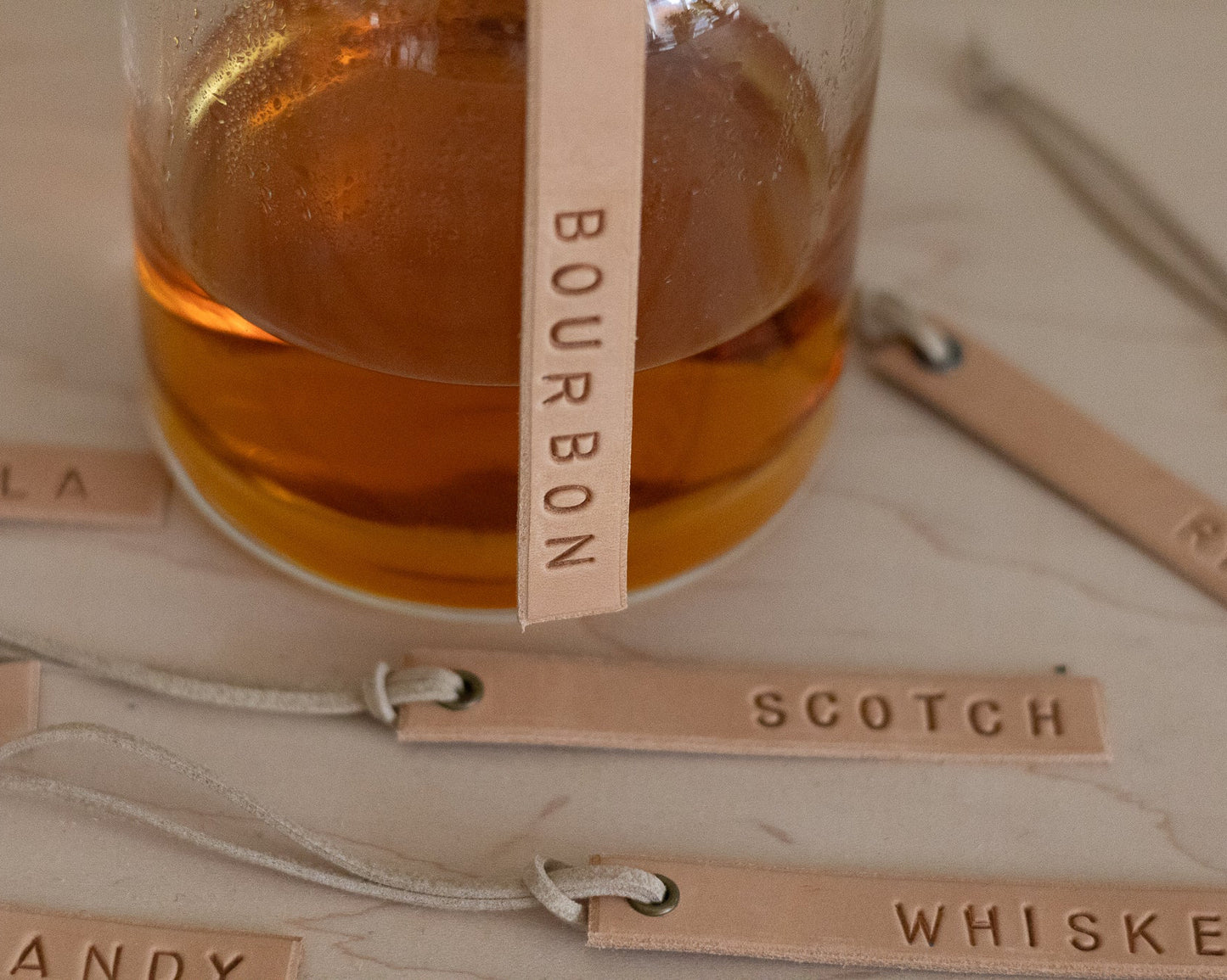 Decanter of bourbon with tags labeled 'Bourbon', 'Scotch', 'Whiskey' on a wooden surface.
