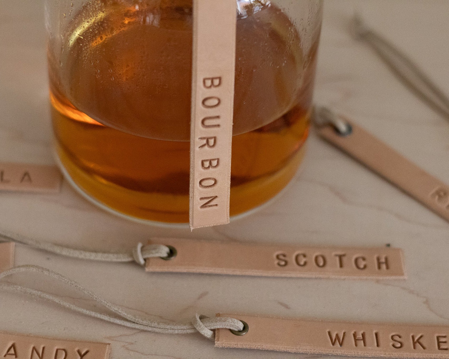 Decanter of bourbon with tags labeled 'Bourbon', 'Scotch', 'Whiskey' on a wooden surface.