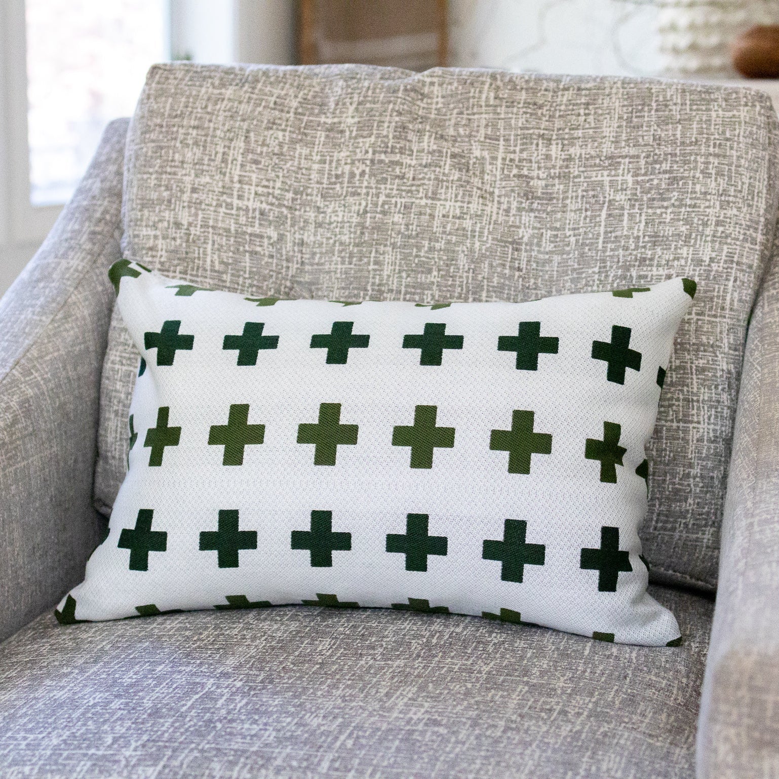 White pillow with green crosses on a gray armchair