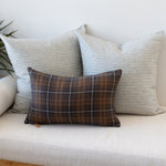 Plaid pillow on a beige bench with two gray pillows and one plaid pillow