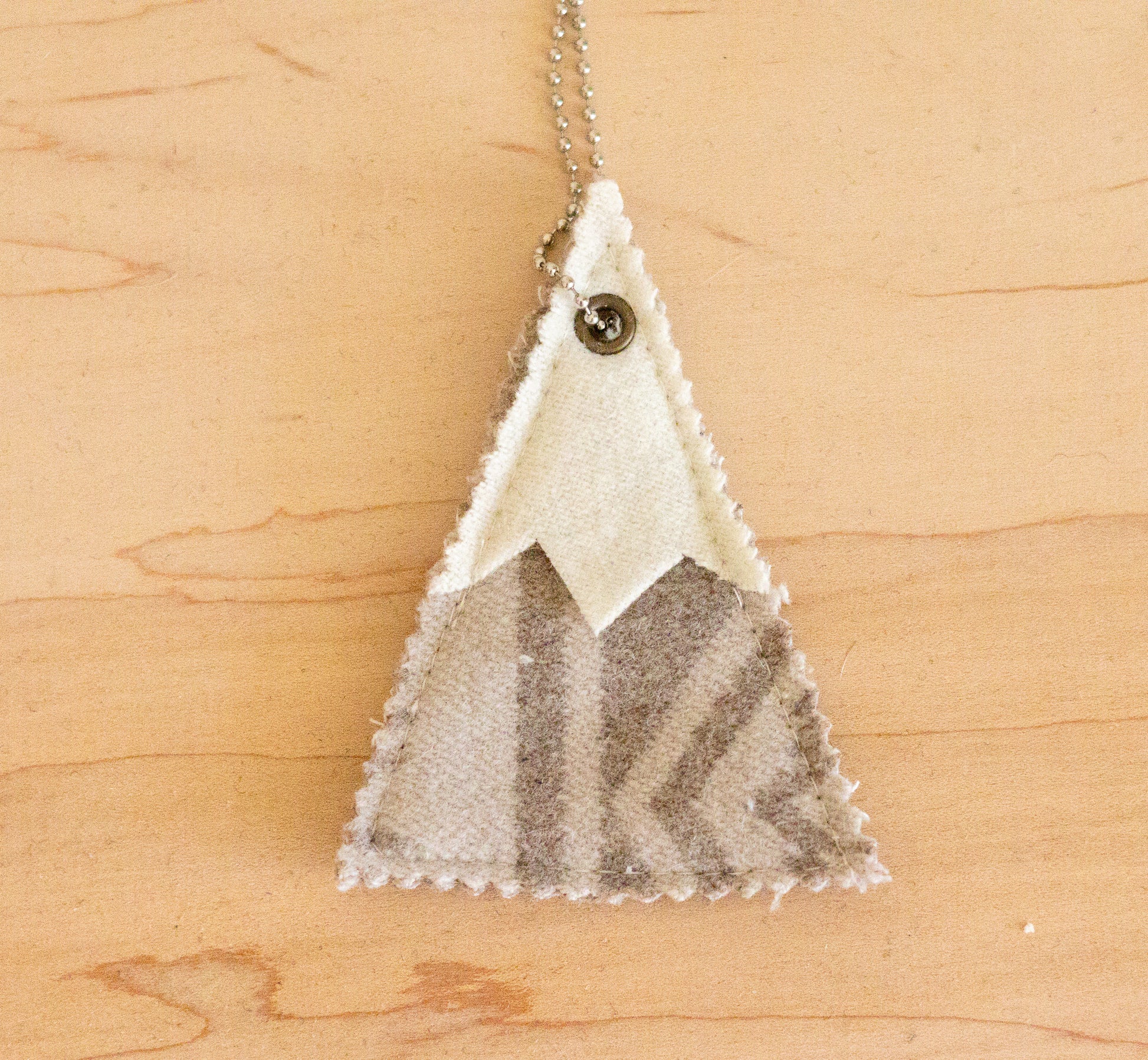 Triangular pendant with mountain design on a wooden surface
