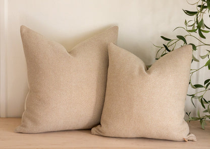Two beige textured pillows on a wooden surface with a plant in the background.