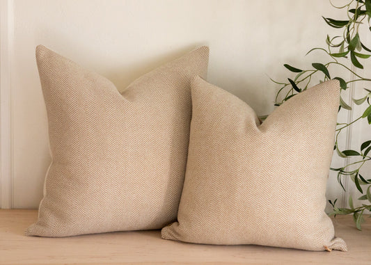 Two beige textured pillows on a wooden surface with a plant in the background.