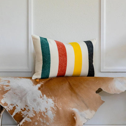 Decorative pillow with striped pattern on a wooden surface with cowhide rug and antlers.