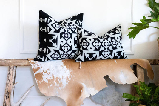 Decorative pillows with black and white patterns on a wooden bench with a cowhide design, against a white wall.