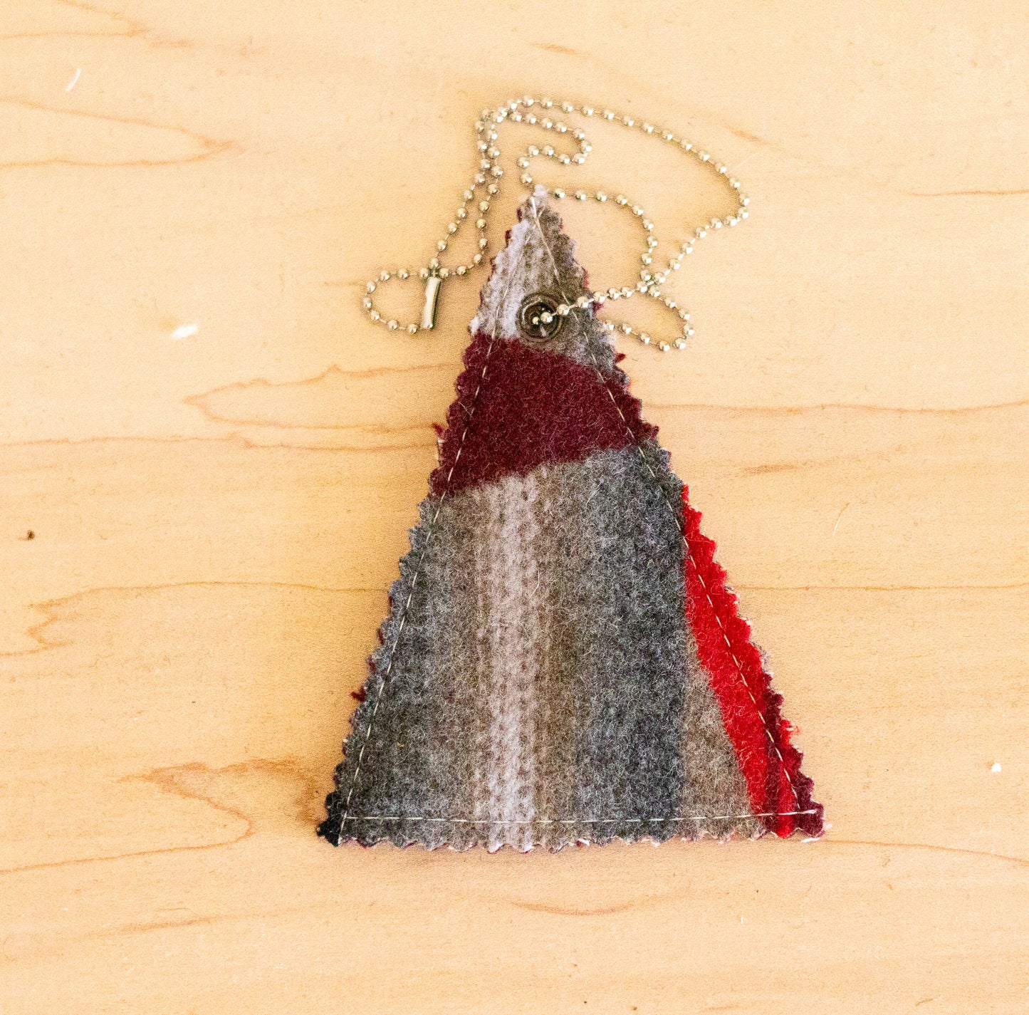 Triangular fabric ornament with red and gray stripes on a wooden surface