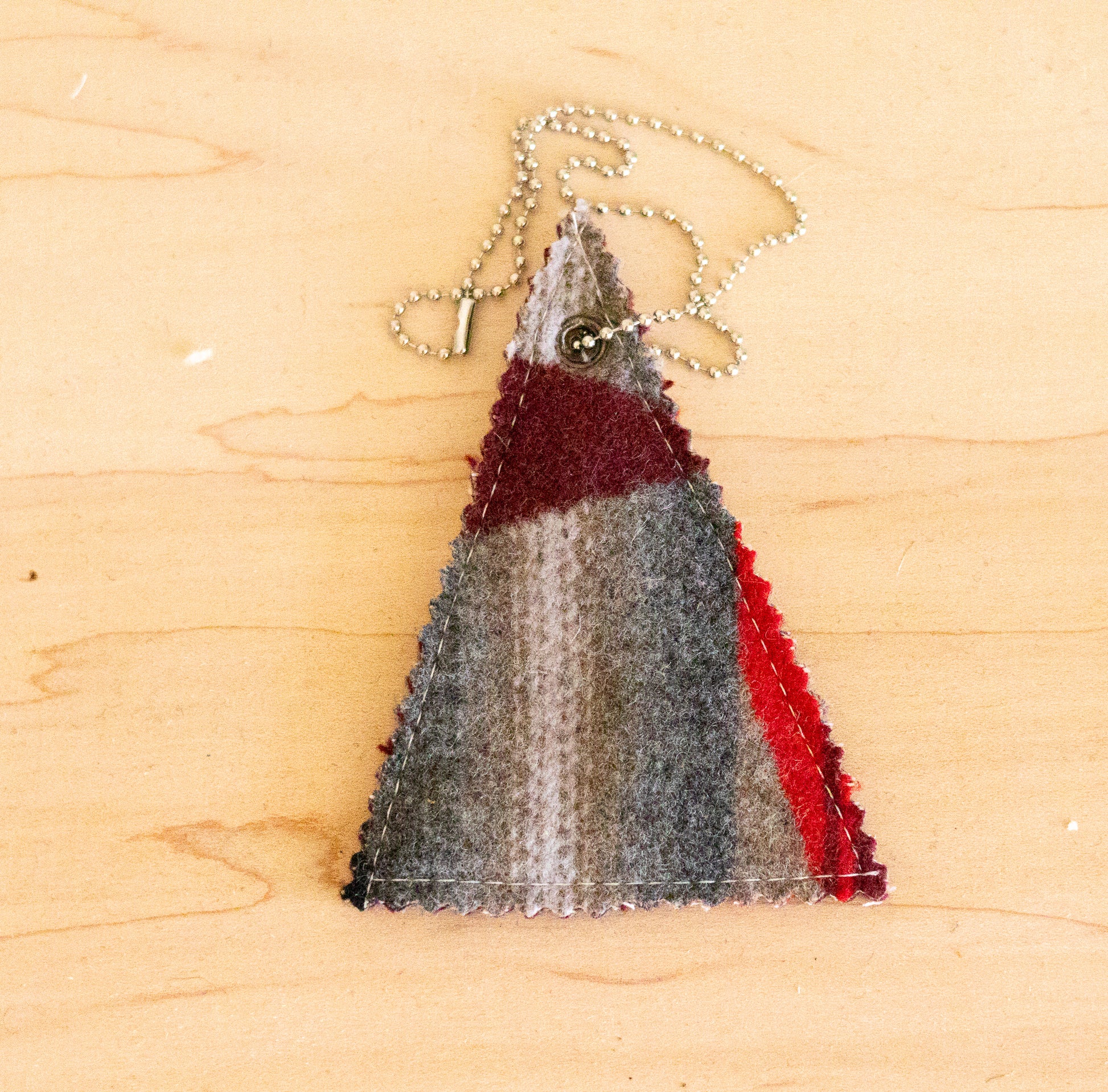 Triangular fabric ornament with red and gray stripes on a wooden surface
