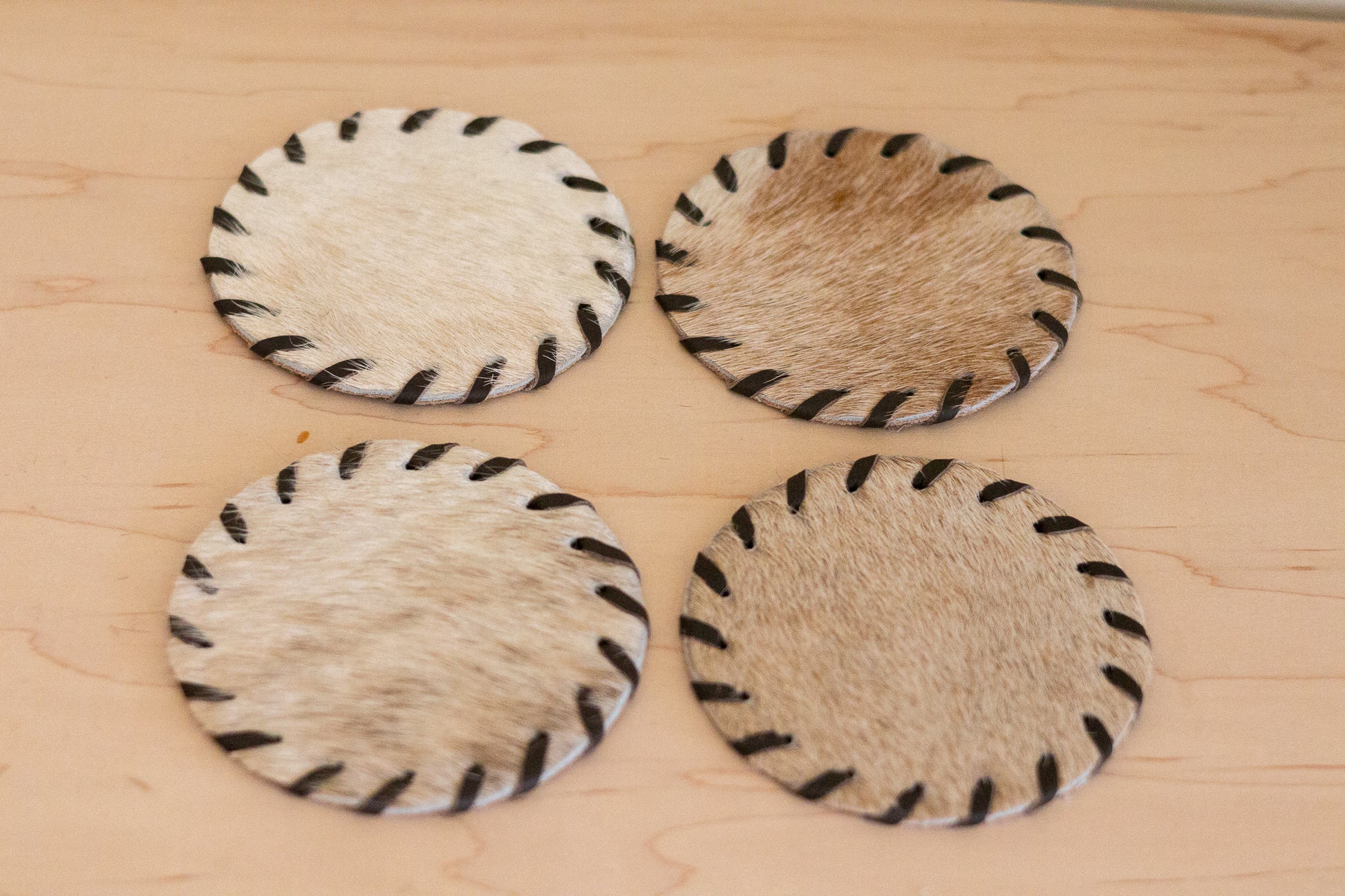 Four hide on hair coasters with black stitching on a wooden surface