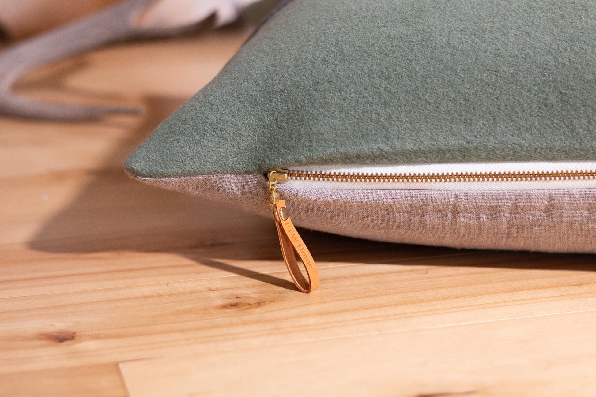 Green pillow cover with a gold zipper on a wooden surface
