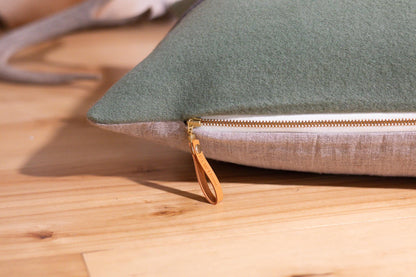 Green pillow cover with a gold zipper on a wooden surface