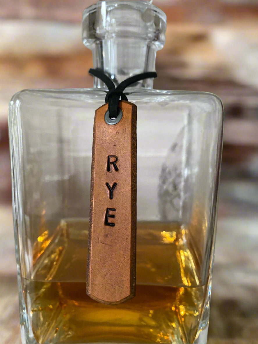 Glass bottle with a leather tag labeled 'RYE' on a blurred background