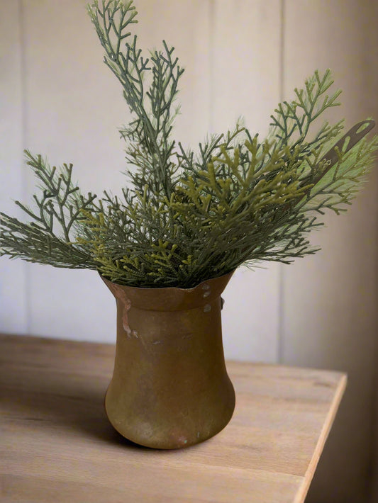 Artificial green plant in a brown pot on a wooden surface with a patterned wall in the background