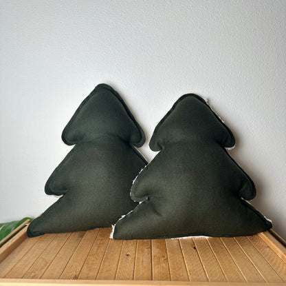 Two dark green triangular pillows on a wooden surface with a light gray wall background