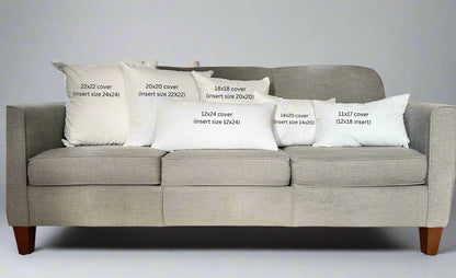 Gray sofa with decorative pillows displaying measurements in a living room setting.