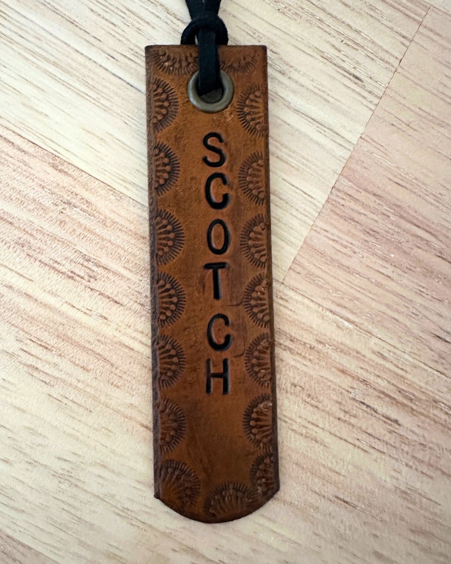 Brown leather tag with 'SCOTCH' engraving on a light wood surface