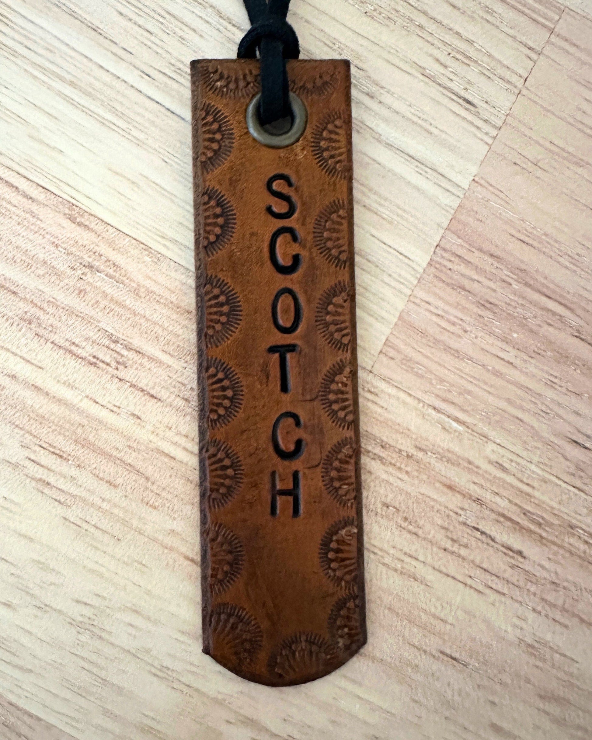 Brown leather tag with 'SCOTCH' engraving on a light wood surface