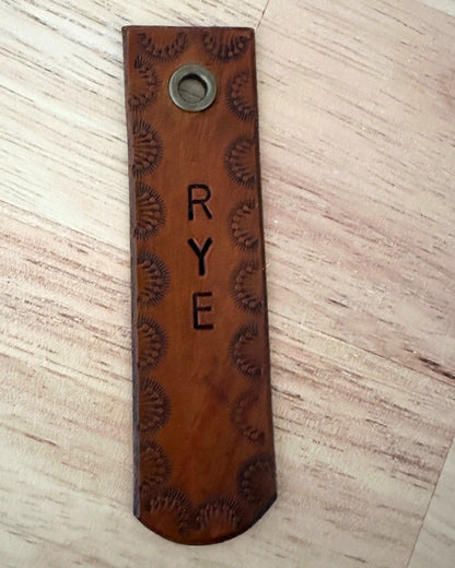 Brown leather tag with 'RYE' engraving on a wooden surface