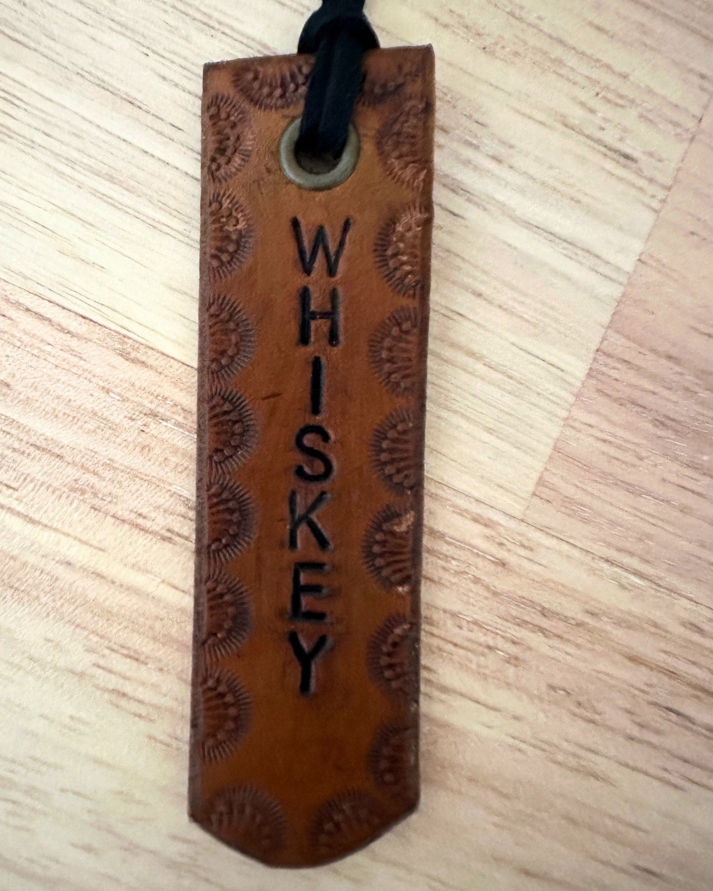 Brown leather tag with 'WHISKEY' engraving on a wooden surface